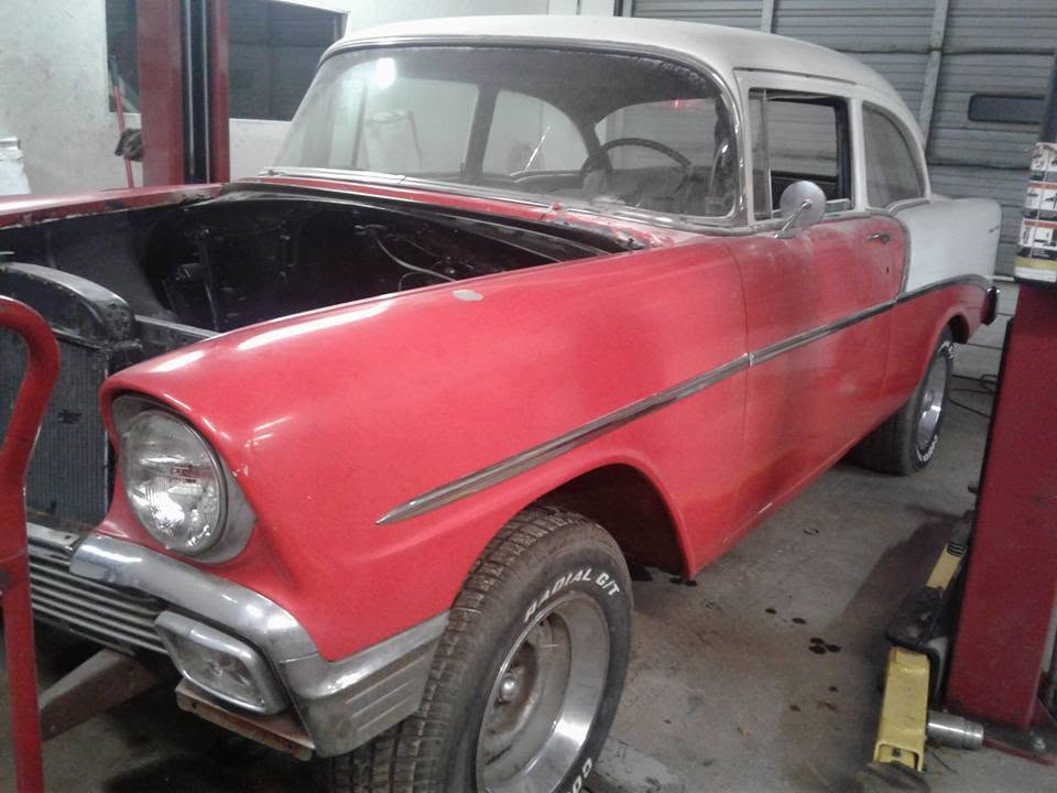 Red and white classic car parked on the shop floor beside a vehicle lift